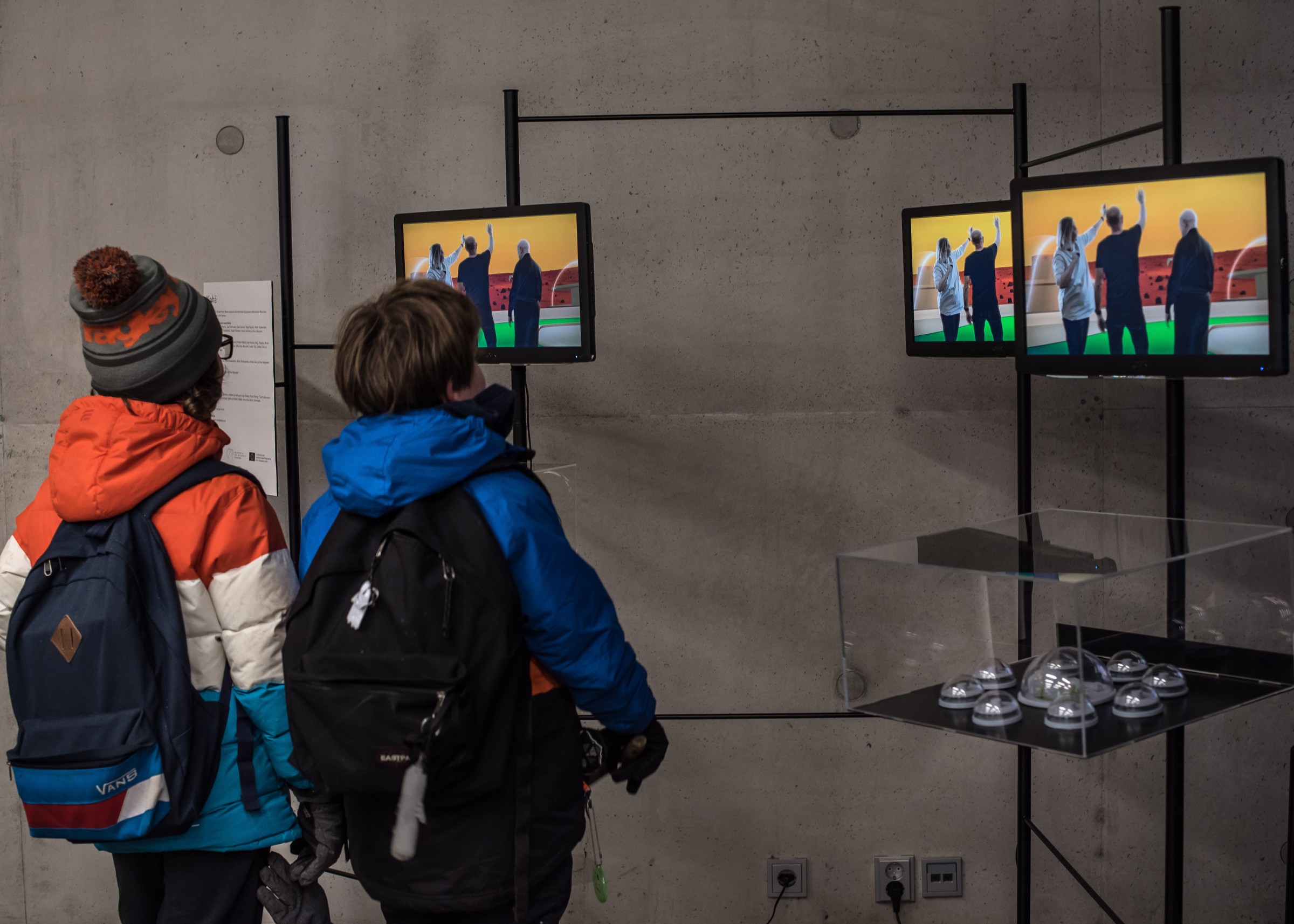 Two boys looking at the screens in the exhibition of Recovered Utopias