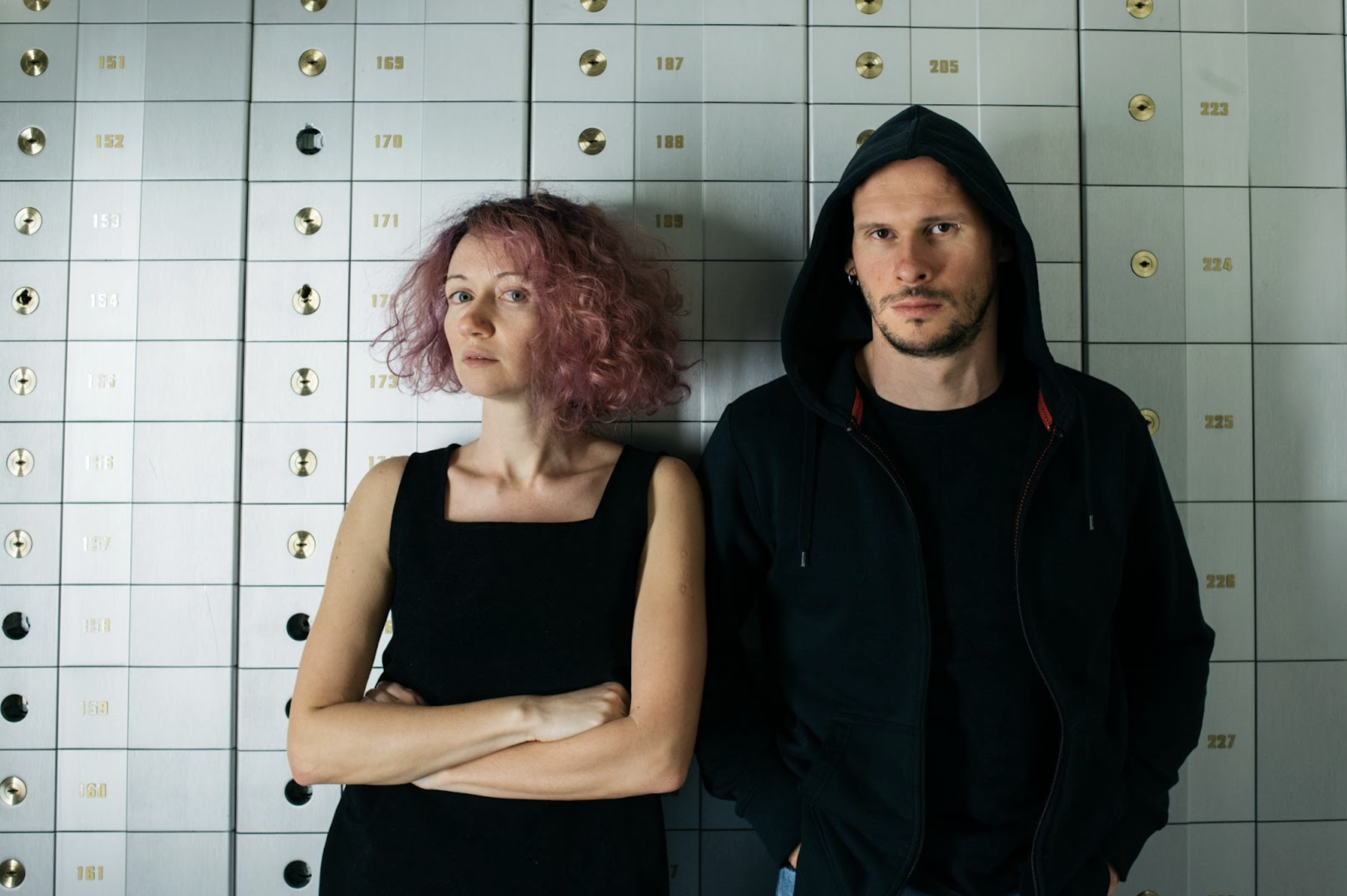 Two people, artist collective eeefff, standing inf front of a white wall, looking at camera, wearing black clothes, with serious faces.